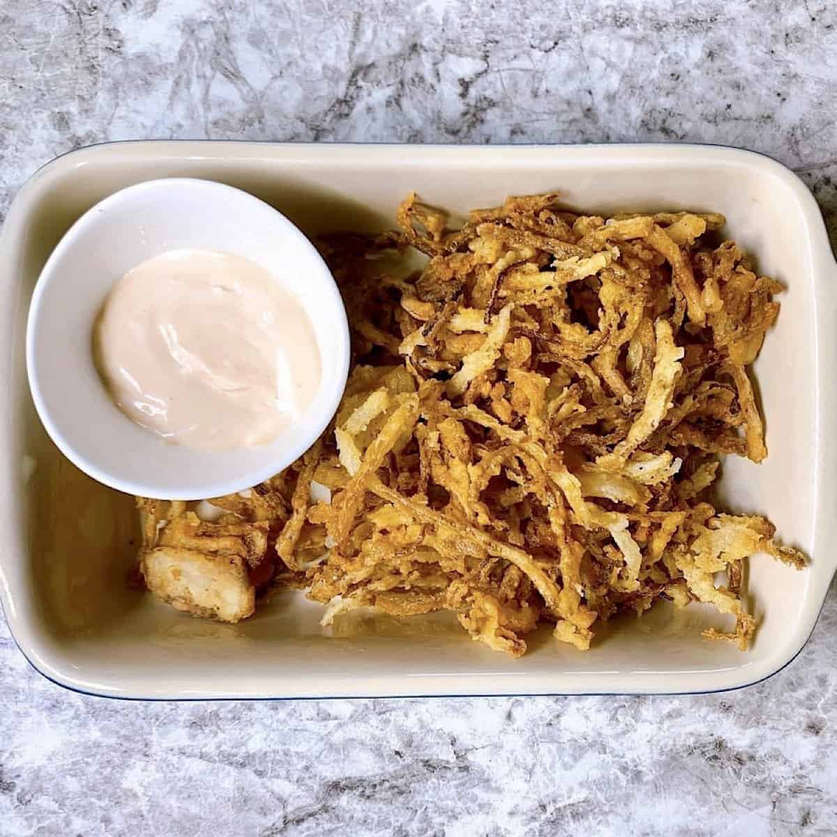 Crispy fried onions in small ceramic crock with dipping sauce