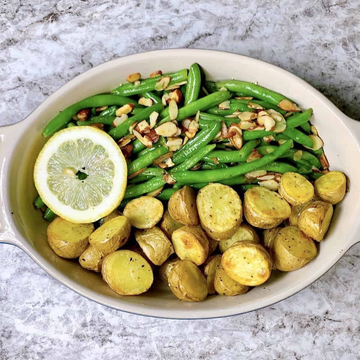 Green beans almondine and potatoes in casserole dish topped with slivered toasted almonds and lemon