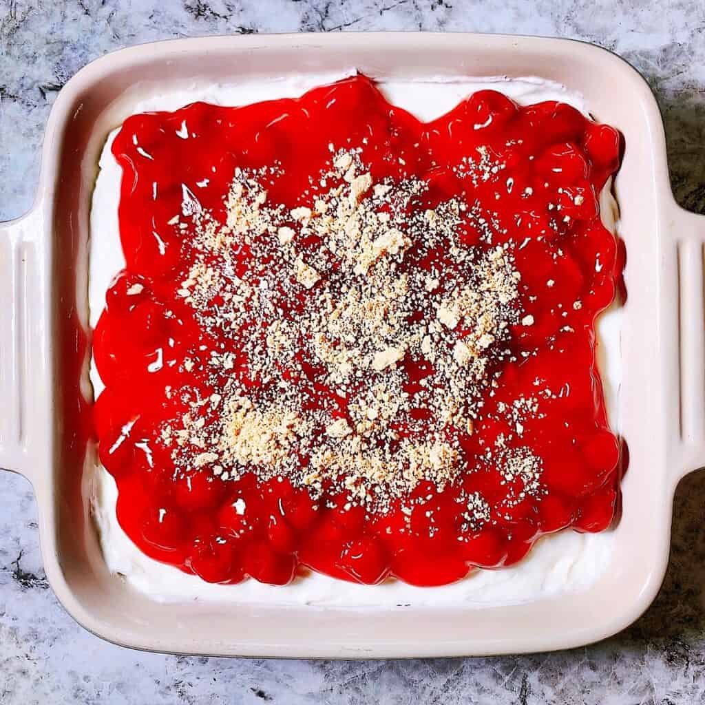 Cherry cheesecake in casserole dish topped with graham cracker crumbs
