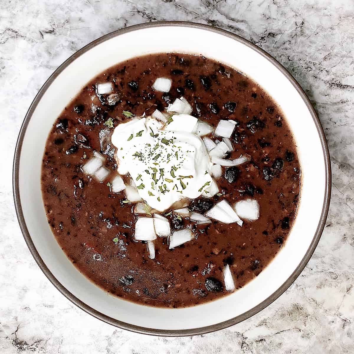 A bowl full of black bean soup with chopped white onion.