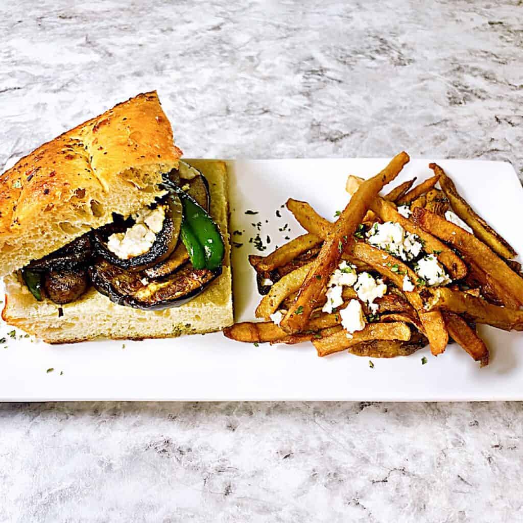 Grilled eggplant sandwich on a plate with French fries topped with feta