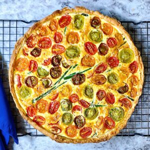 A quiche with roasted tomatoes and asparagus on a bakers rack