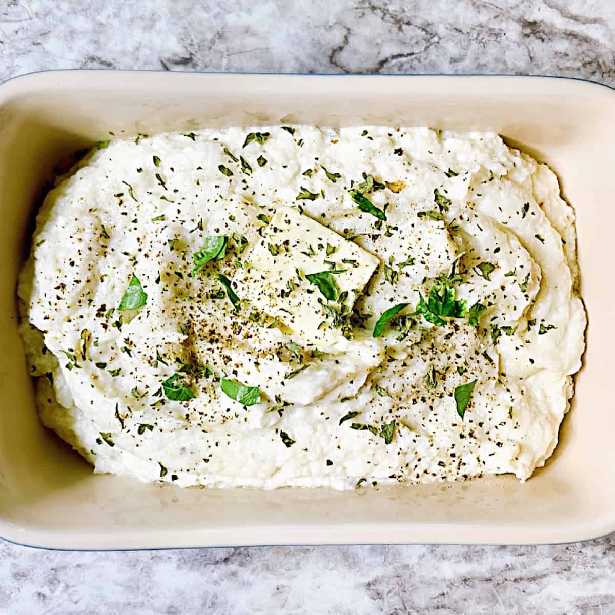 A casserole dish filled with cauliflower mashed potatoes with butter and chives on top