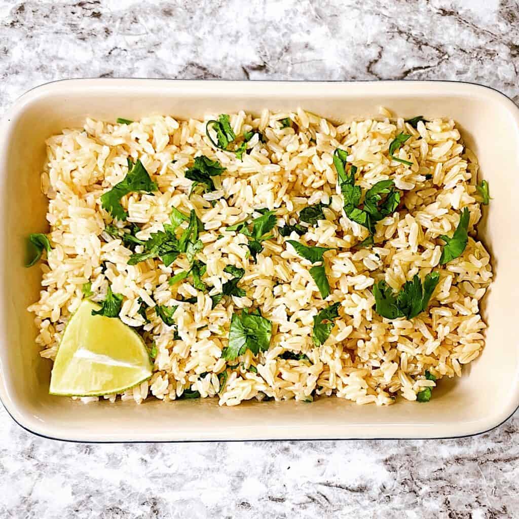 A casserole dish filled with fresh cilantro brown rice and topped with lime