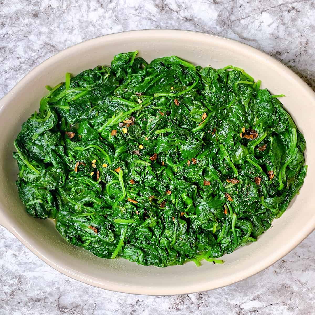 Casserole dish filled with sautéed spinach and crushed red pepper