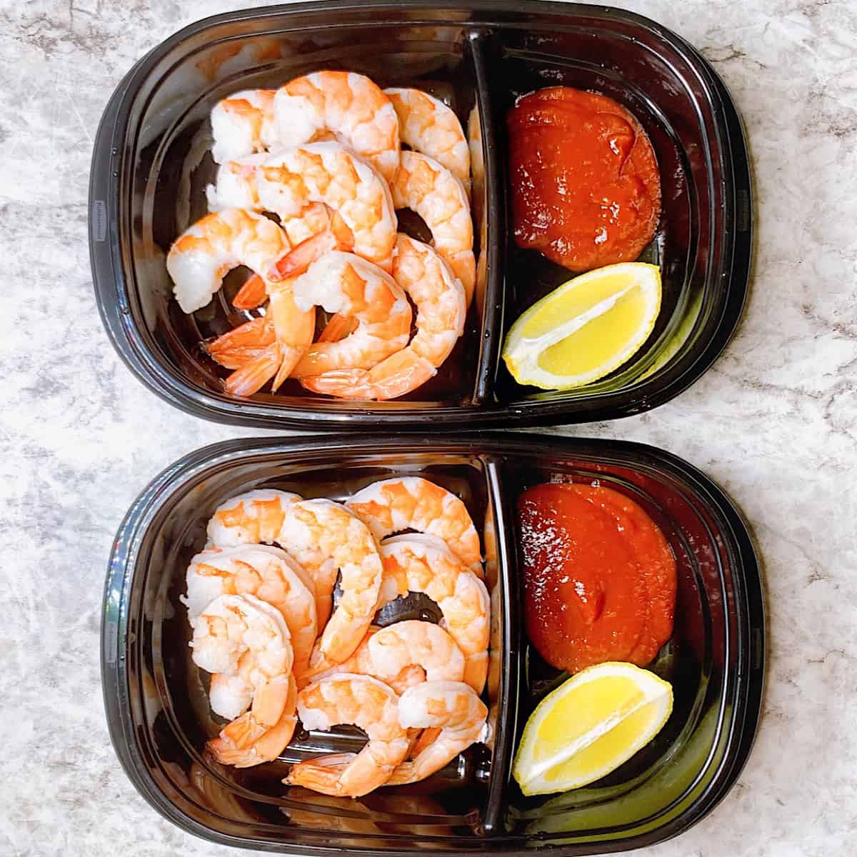 Two meal prep containers with jumbo shrimp cocktail , lemon wedges, and cocktail sauce