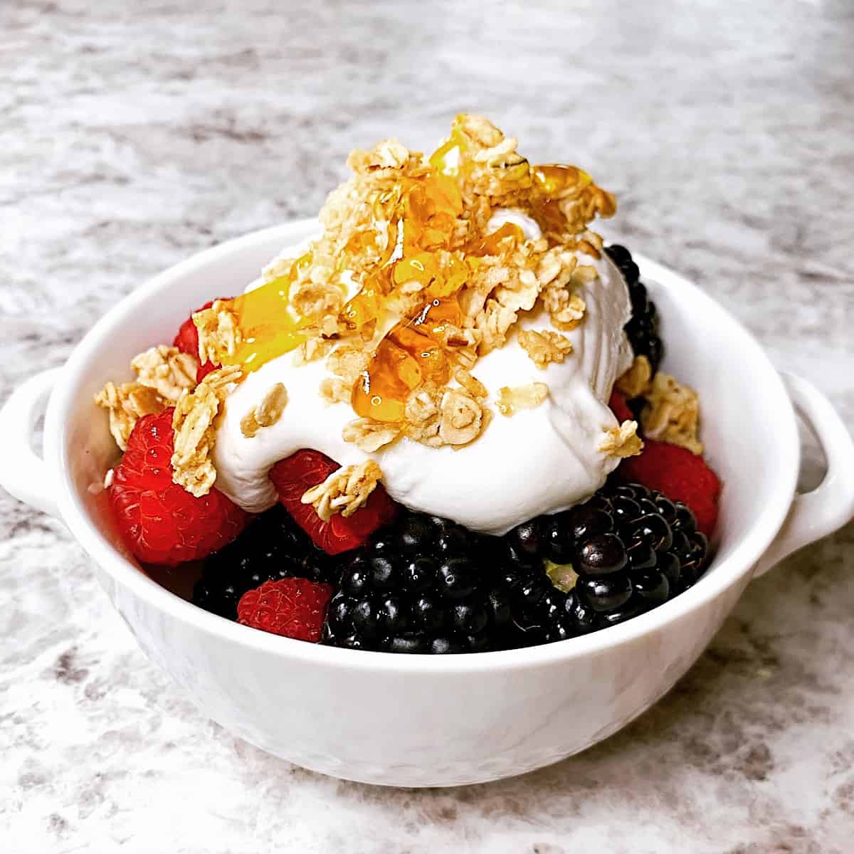 Small bowl filled with blueberries blackberries and raspberries topped with yogurt granola and honey