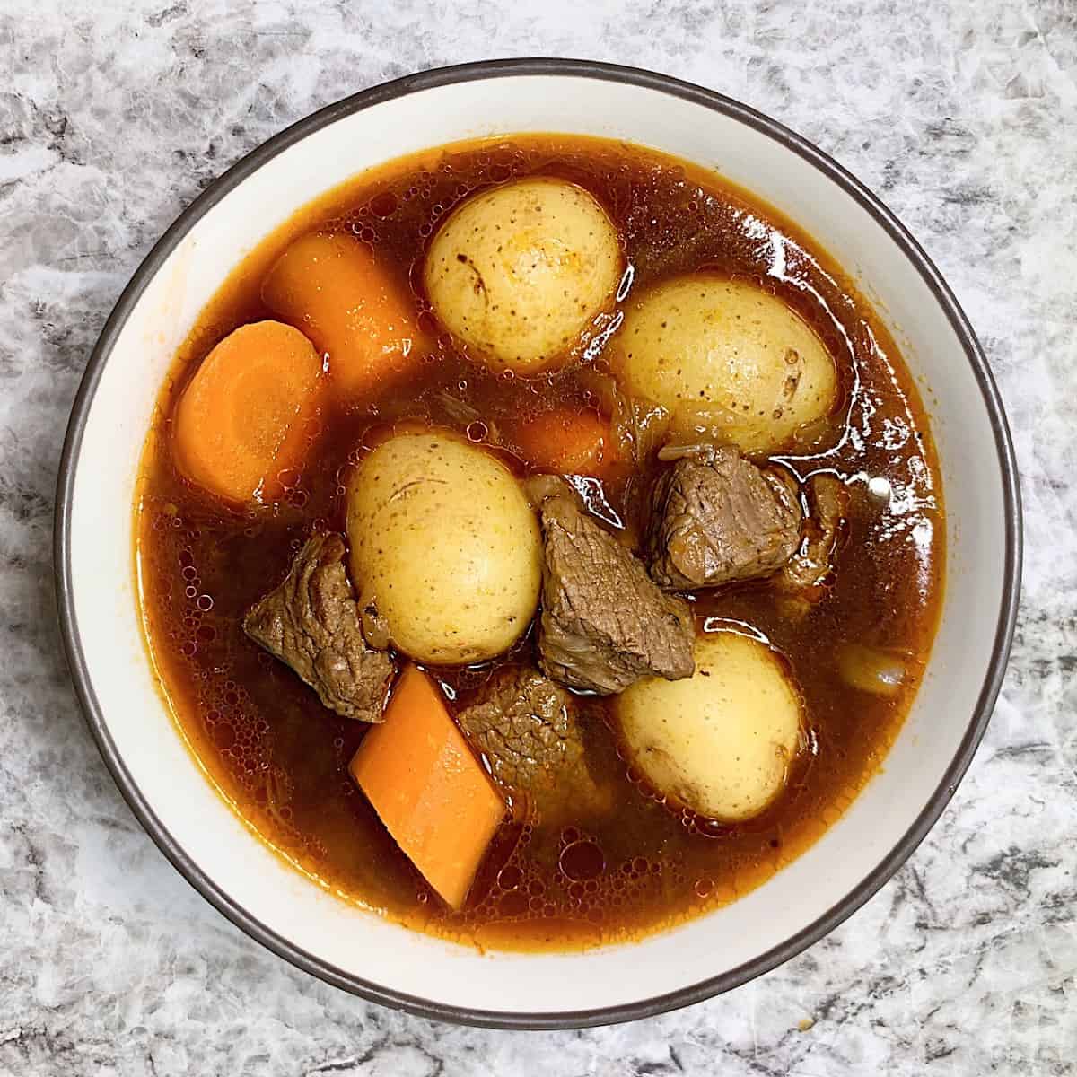 Beef stew with carrots potatoes stew meat and onion in a bowl includes Guinness Beer in recipe