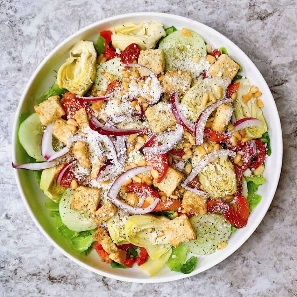 Large salad filled with roasted red peppers artichoke cucumber red onion parmesan croutons toastedpinenuts