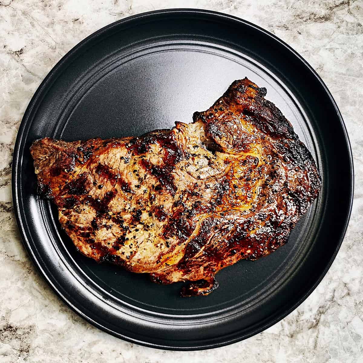 Black plate with large grilled ribeye steak