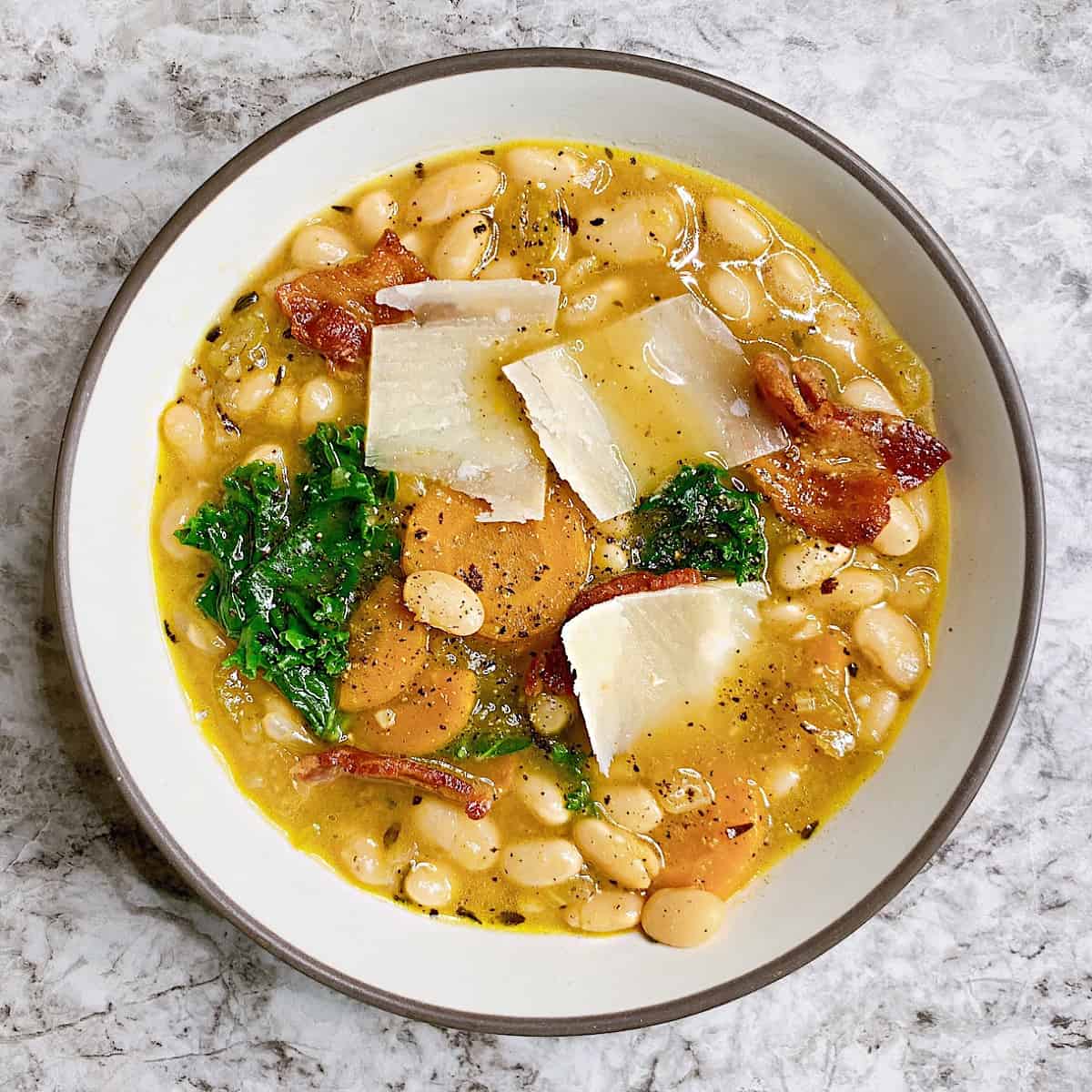 Bowl of white bean soup with bacon kale and parmesan