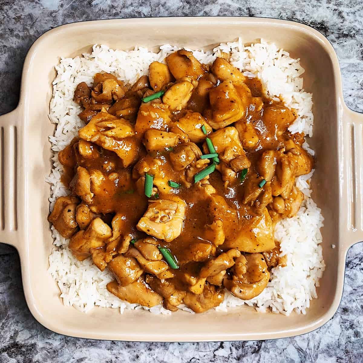 Bourbon chicken over rice with green onion garnish in casserole dish