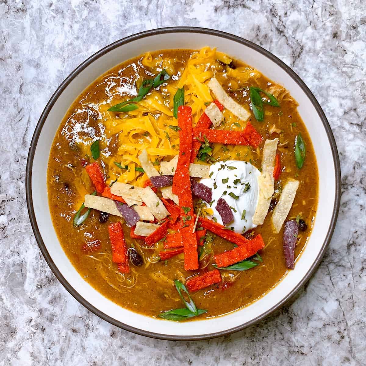 Chicken enchilada soup with tortilla strip cheese and sour cream garnish in soup bowl