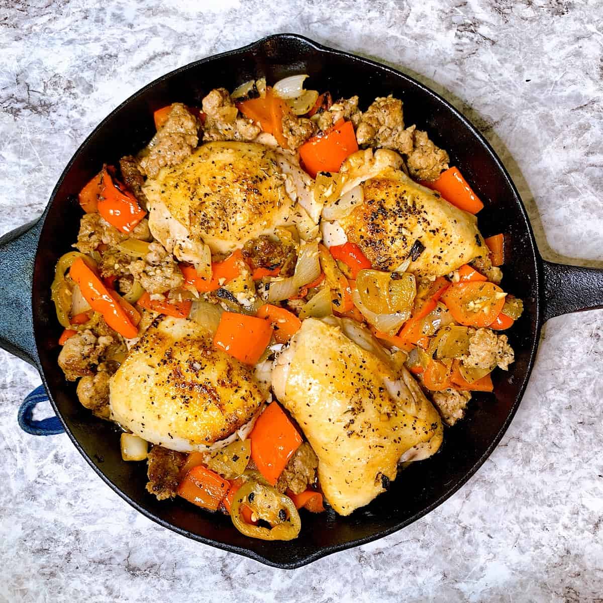 Chicken Scarpariello Four thighs in a cast iron skillet with peppers and juices