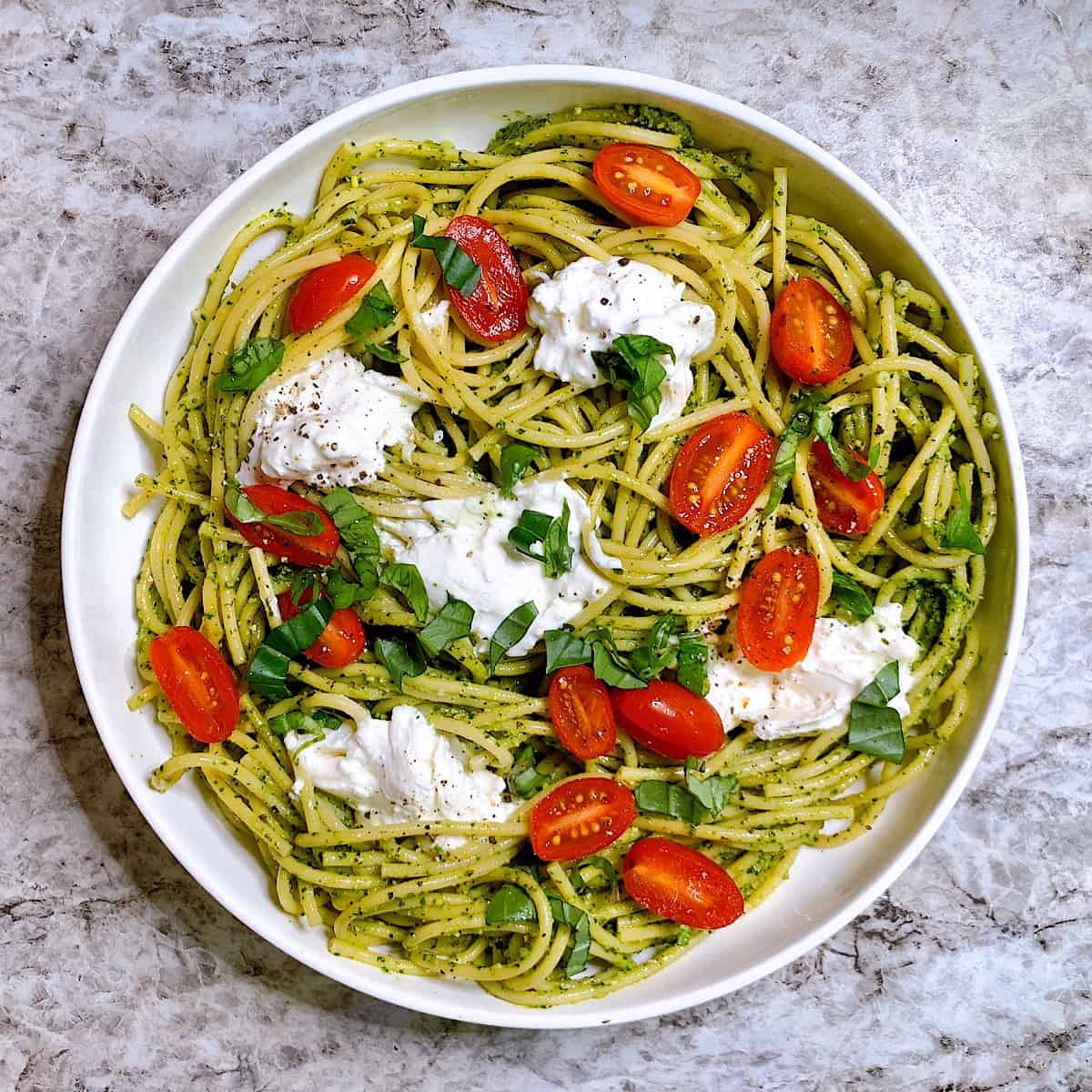 Pesto Bucatini with torn bits of burrata in large pasta dish