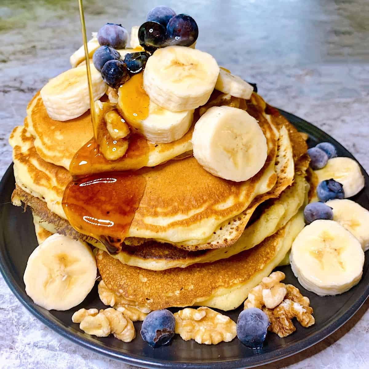 Stack of fluffy pancakes with bananas blueberries walnuts and maple syrup