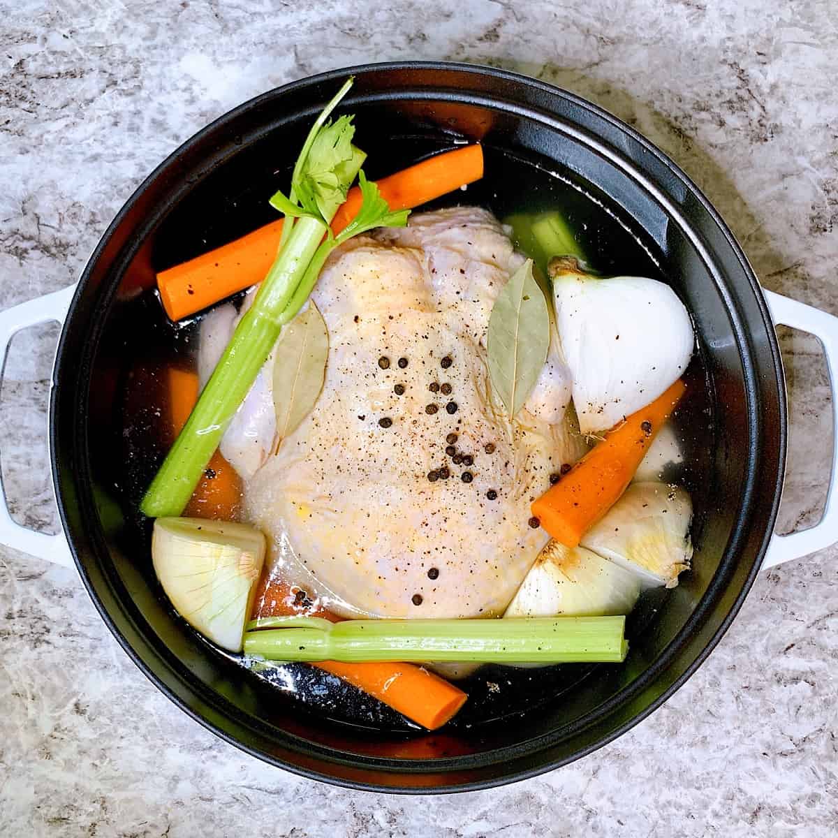 Whole Chicken Fryer in pot with onion carrots celery peppercorn bayleaves