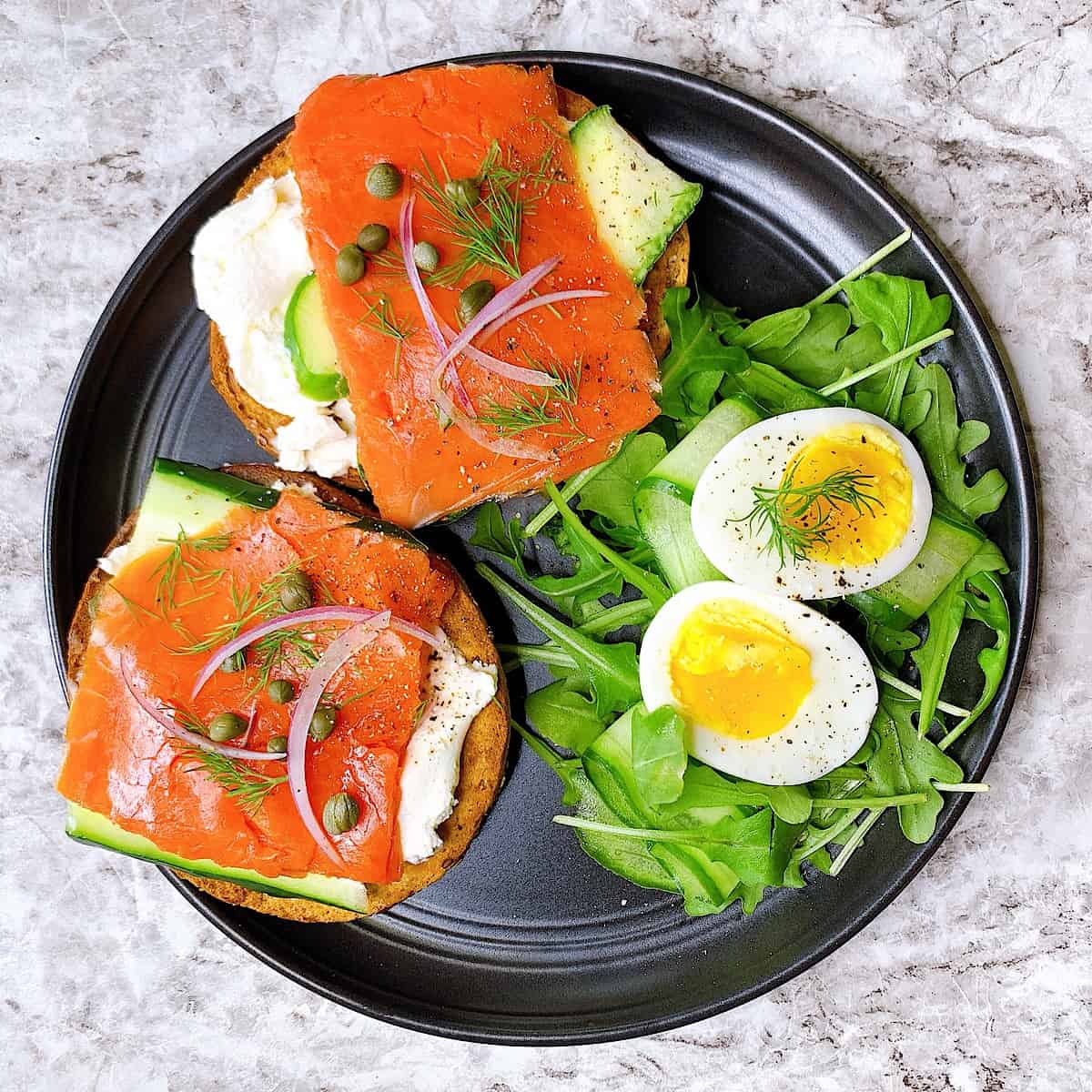 Bagel and lox topped with caper and an arugula side salad and egg