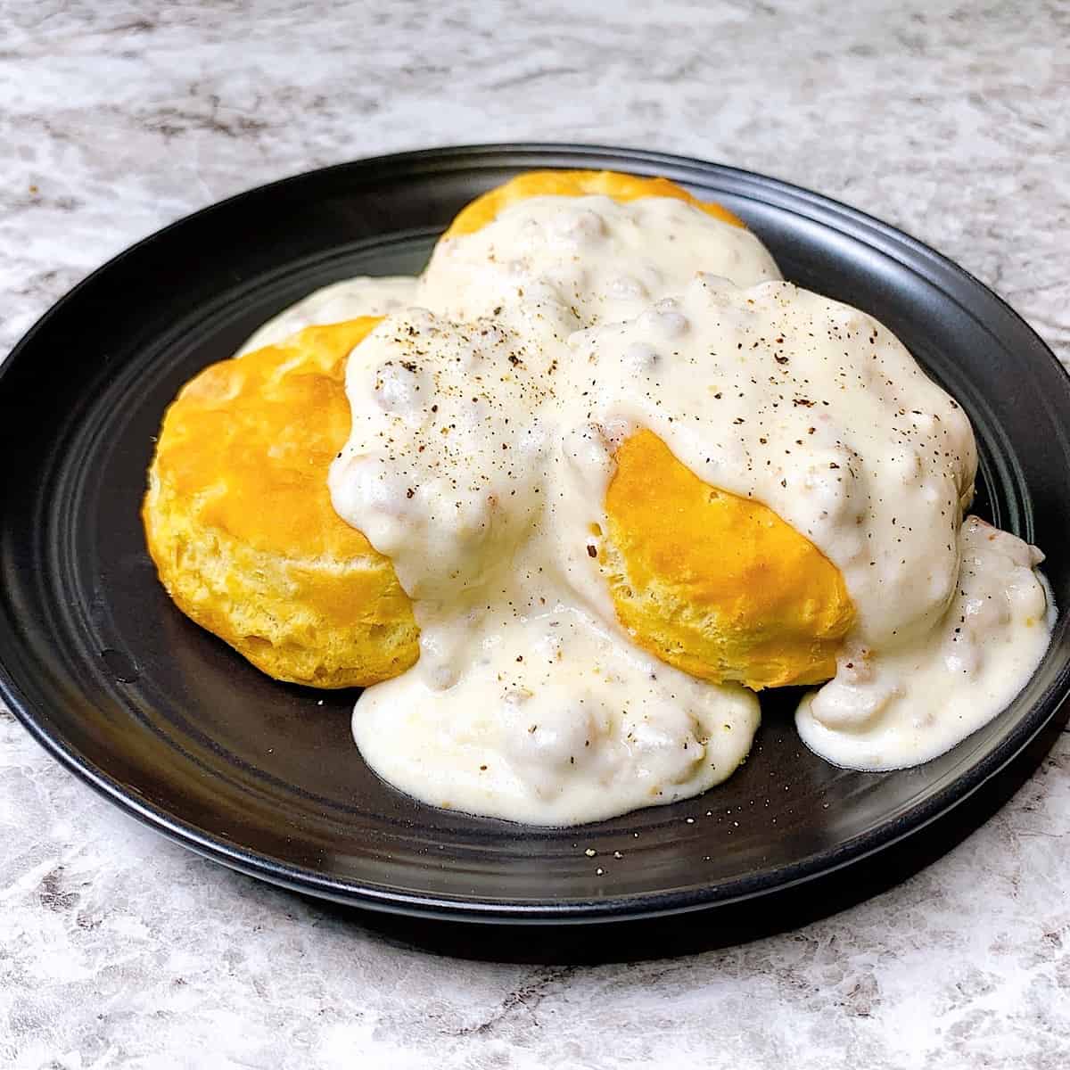 Biscuits on a black plate drenched in sausage gravy