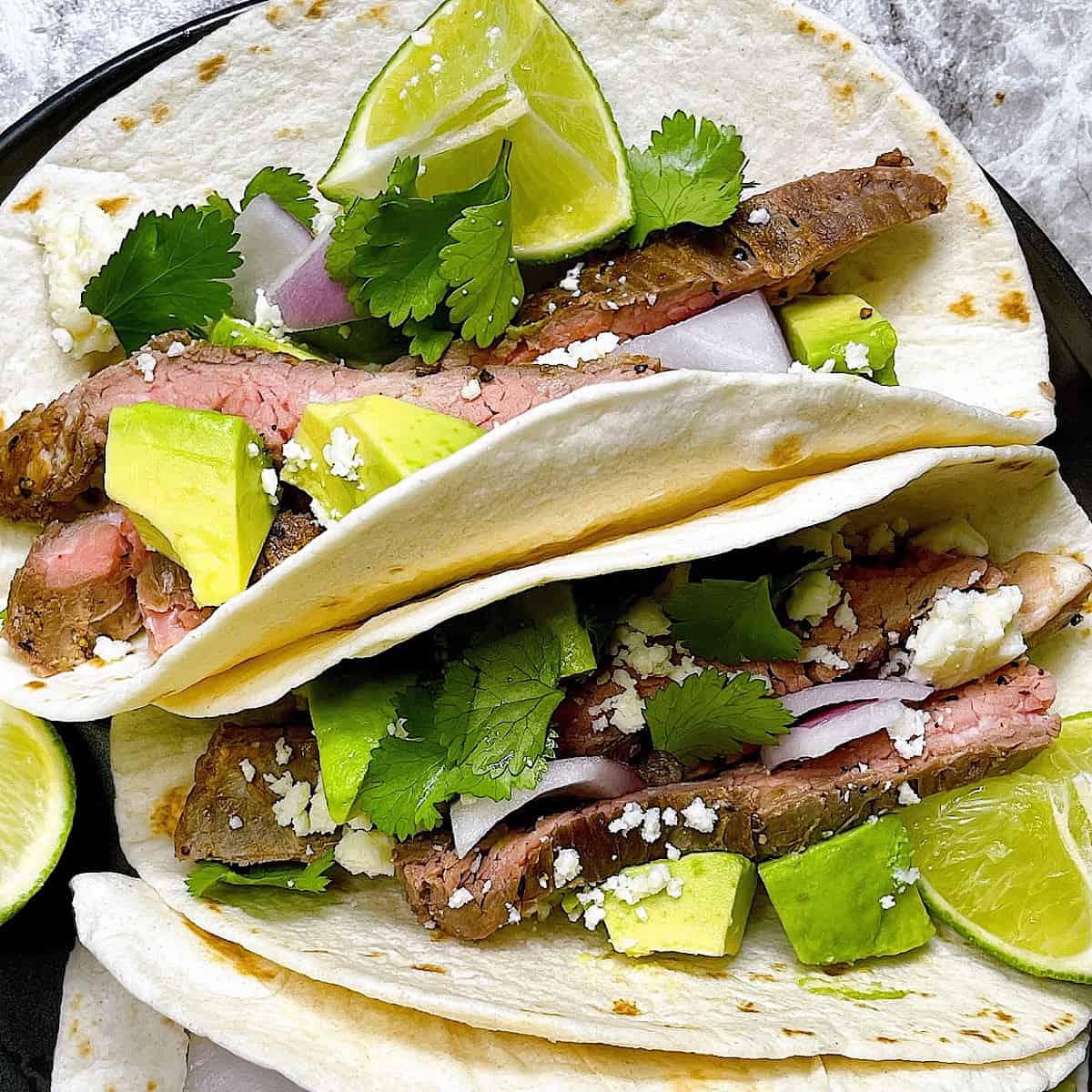 Carne Asada tacos topped with cilantro avocado and cojita cheese