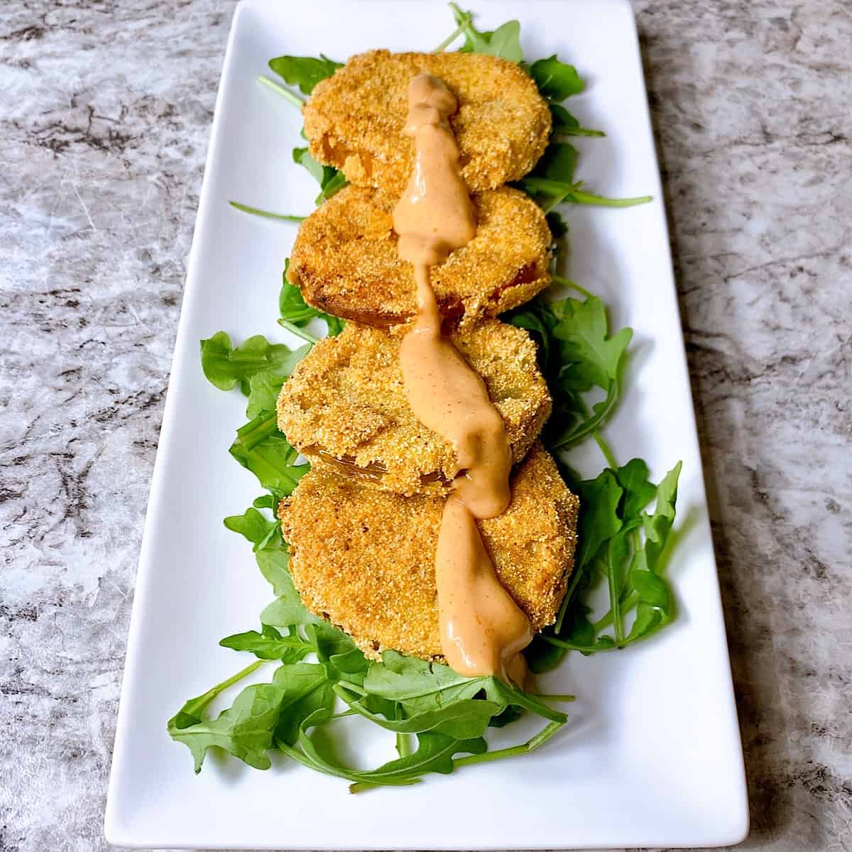Fried Green Tomatoes stacked on plate over a bed of greens and topped with sauce