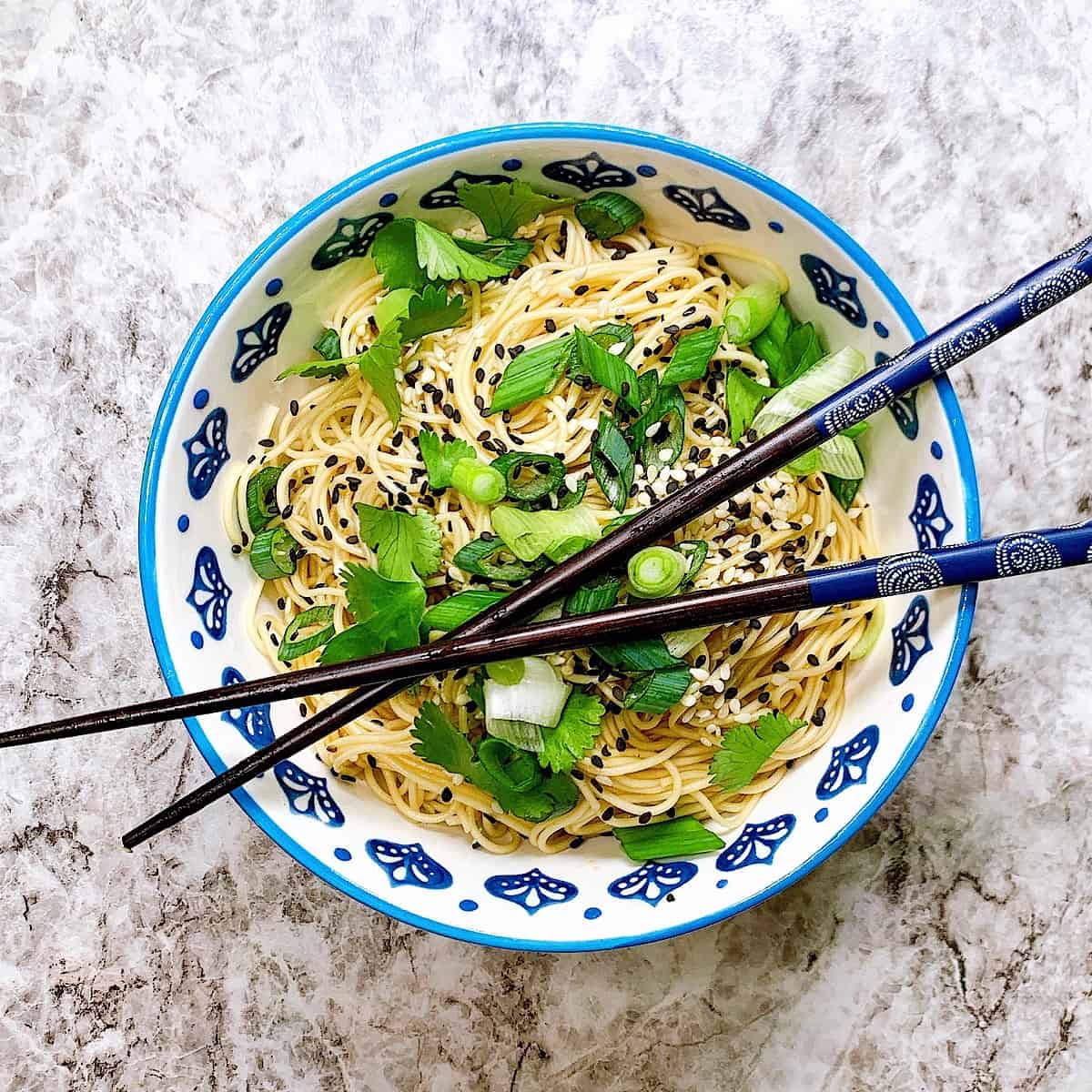Soba noodle salad in bowl with chopsticks topped with sesame seeds and cilantro