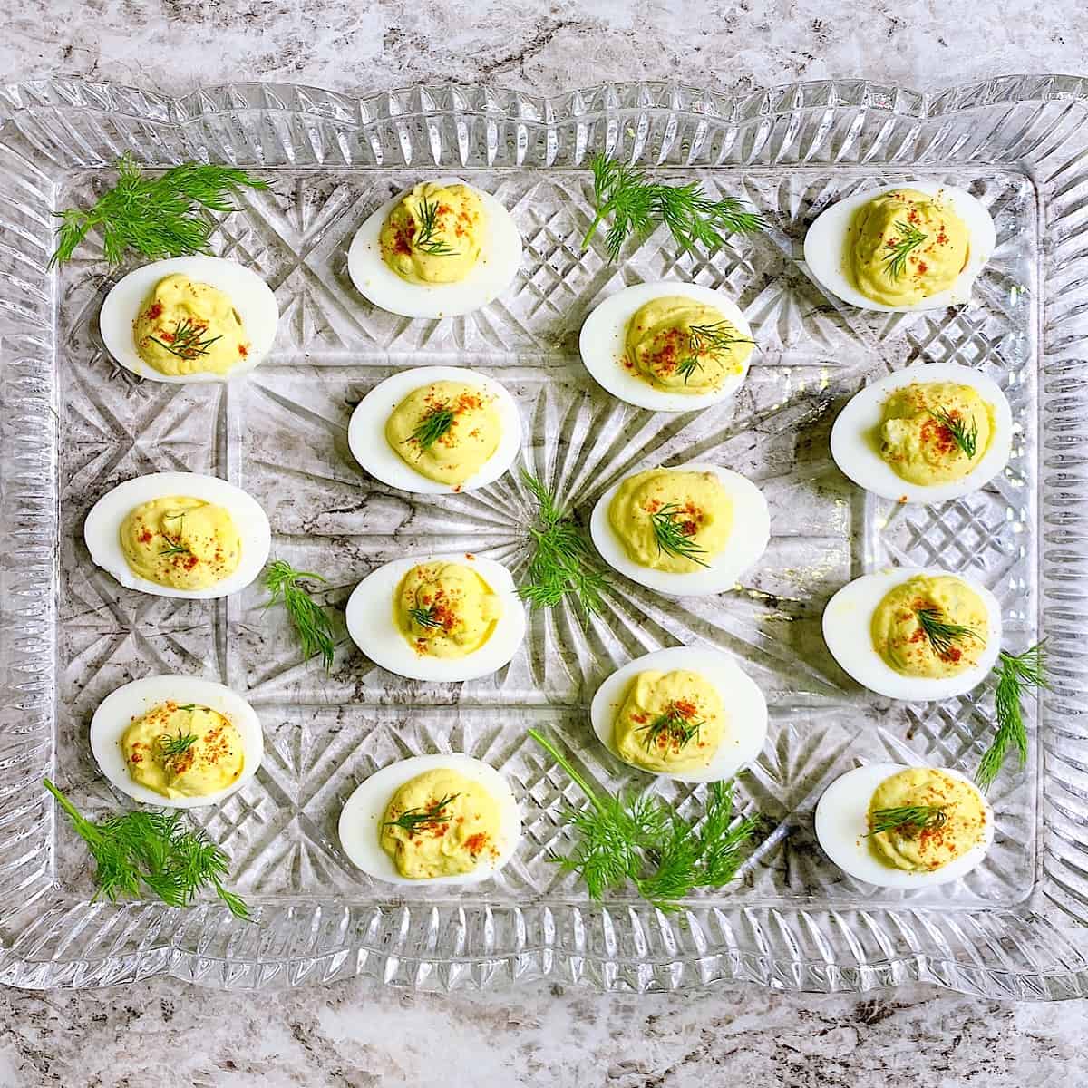 Deviled eggs on a crystal platter topped with paprika and dill