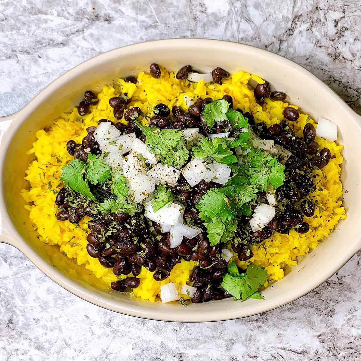 a casserole dish filled with yellow rice black beans onion and cilantro on top