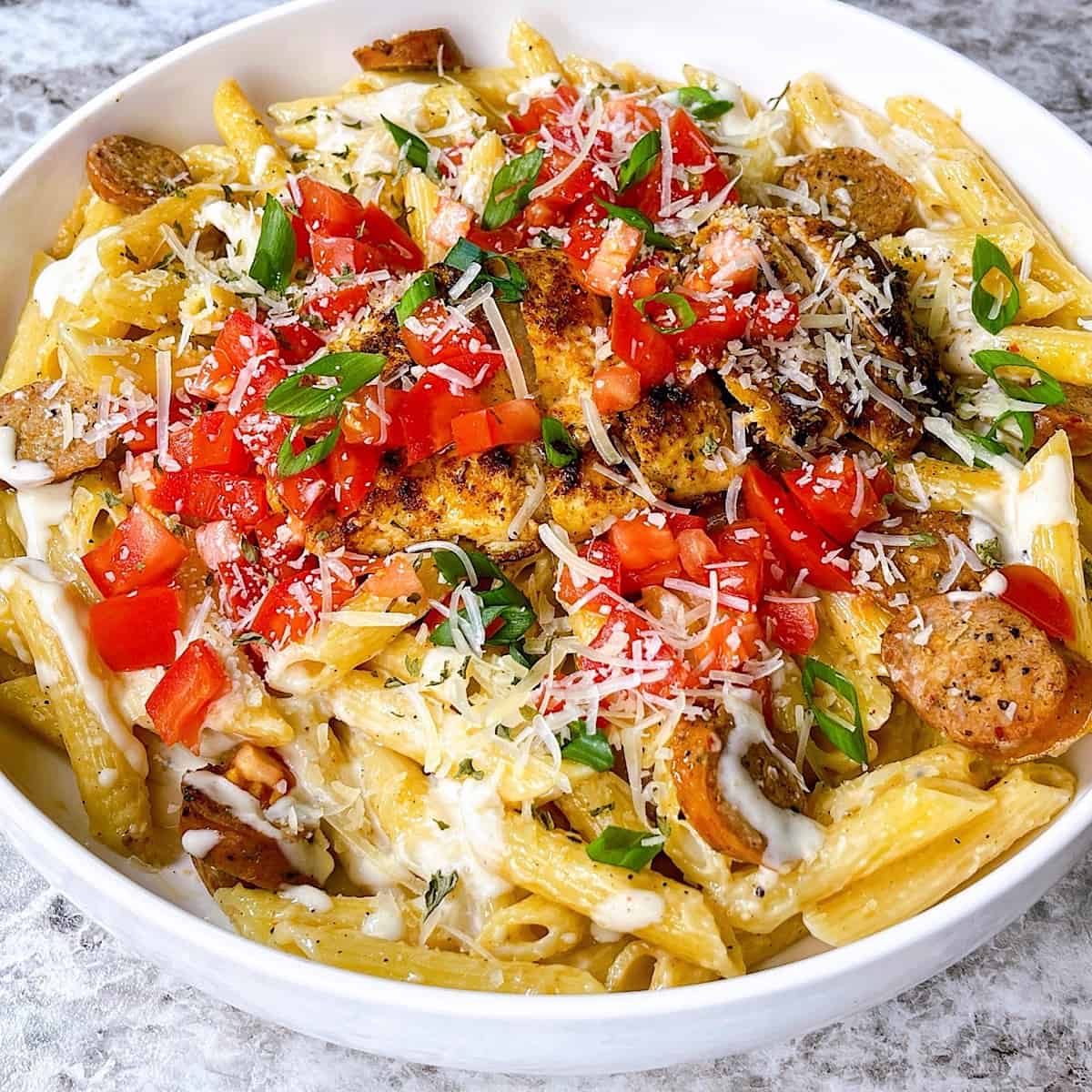 Creamy Cajun chicken pasta topped with tomato, parmesan, and green onion