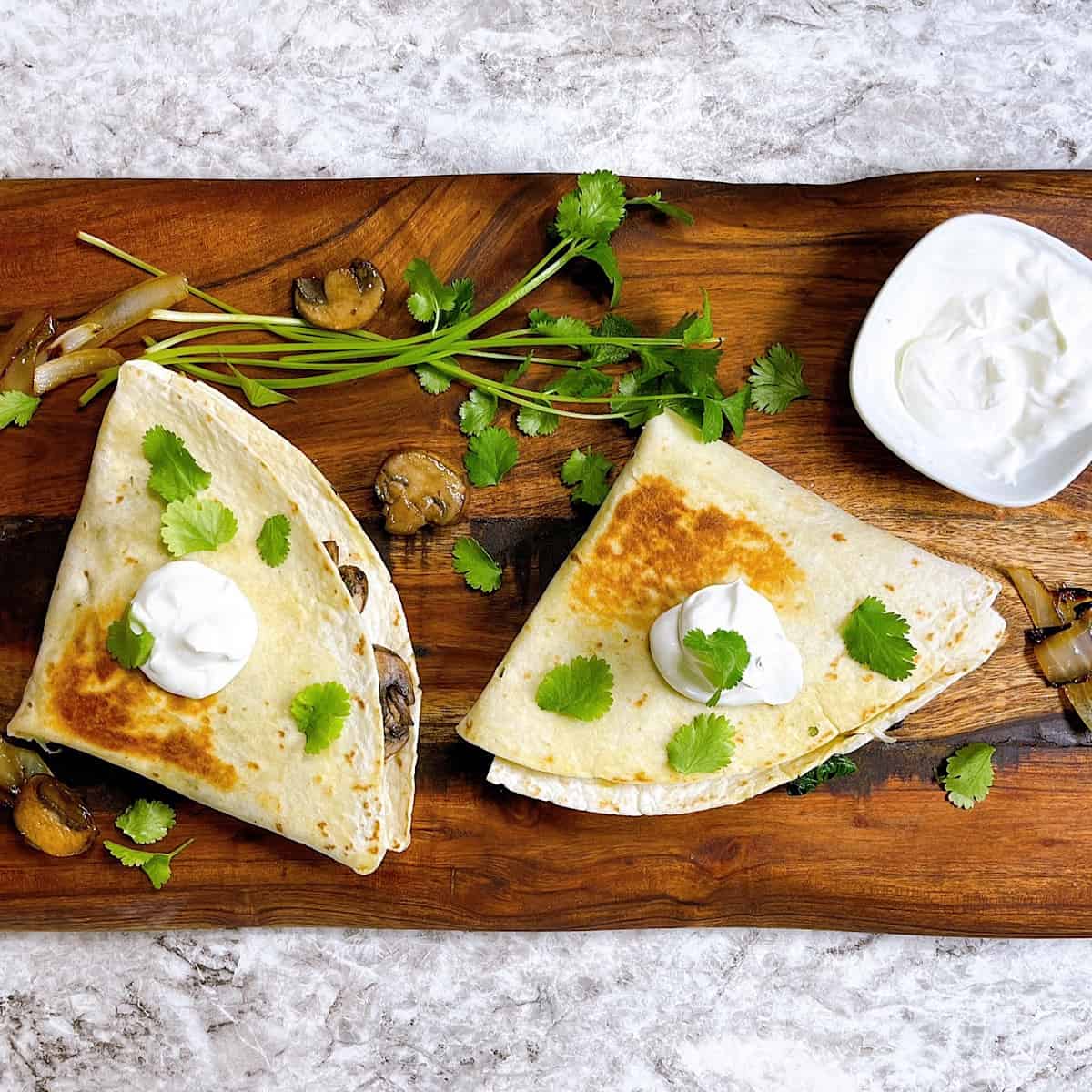 Spinach and mushroom quesadillas on cutting board topped with sour cream and cilantro
