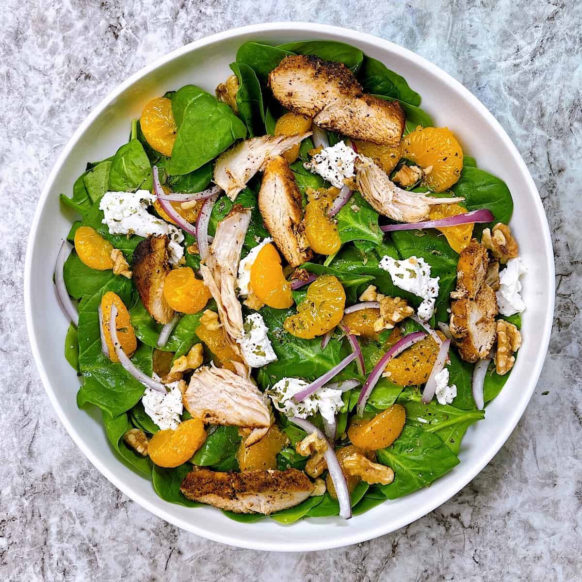 Orange spinach salad with chicken in large white salad bowl