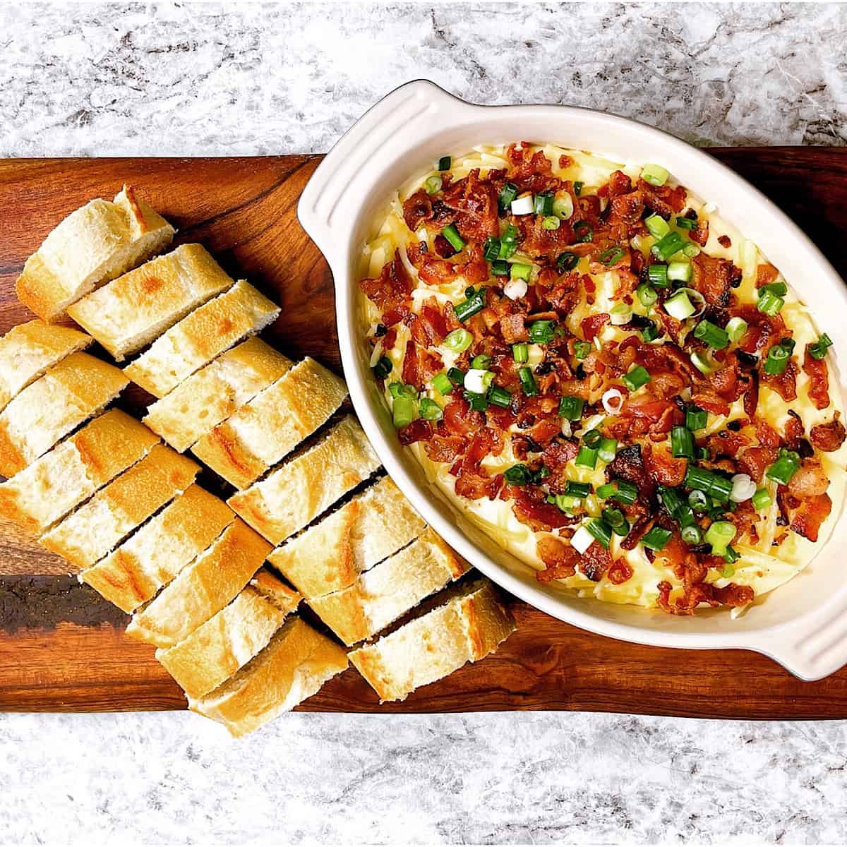 Smoked Gouda and white cheddar dip in bowl on cutting board with French bread