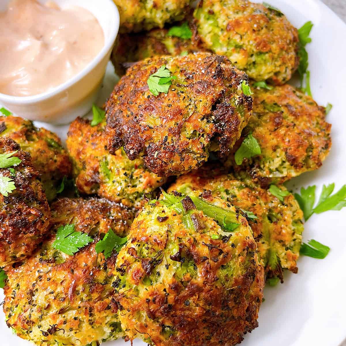 Clean Eating Broccoli Cheese Air Fryer Patties in bowl with spicy sauce and garnished with parsley