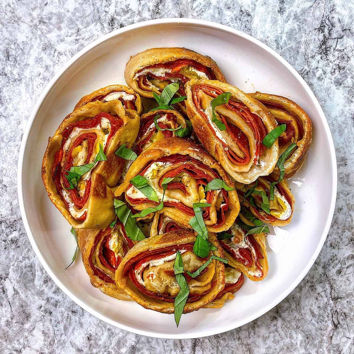 Pepperoni rolls sliced on platter with parmesan, Italian seasoning, and basil