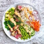 Seared ahi tuna poke bowl with spicy sauce and garnishes in a white bowl.