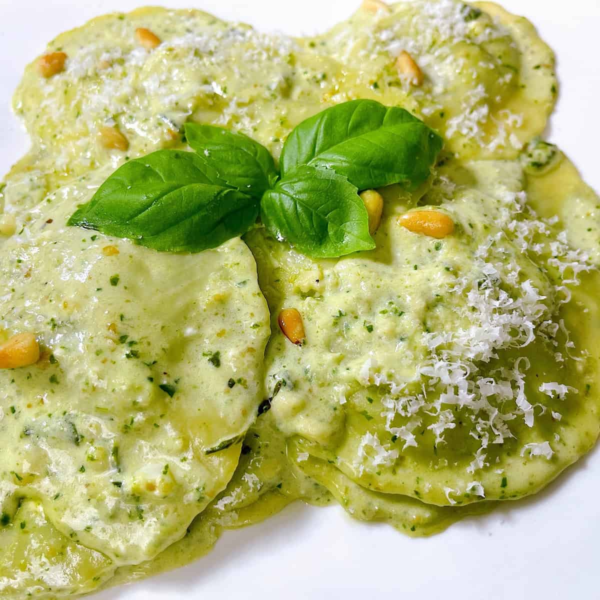 Spinach Ravioli with Pesto Cream Sauce​ topped with Parmesan and basil leaves