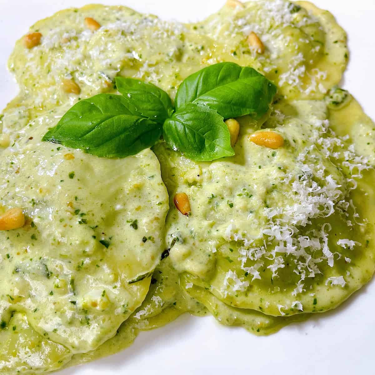 Spinach Ravioli with Pesto Cream Sauceโ topped with Parmesan and basil leaves