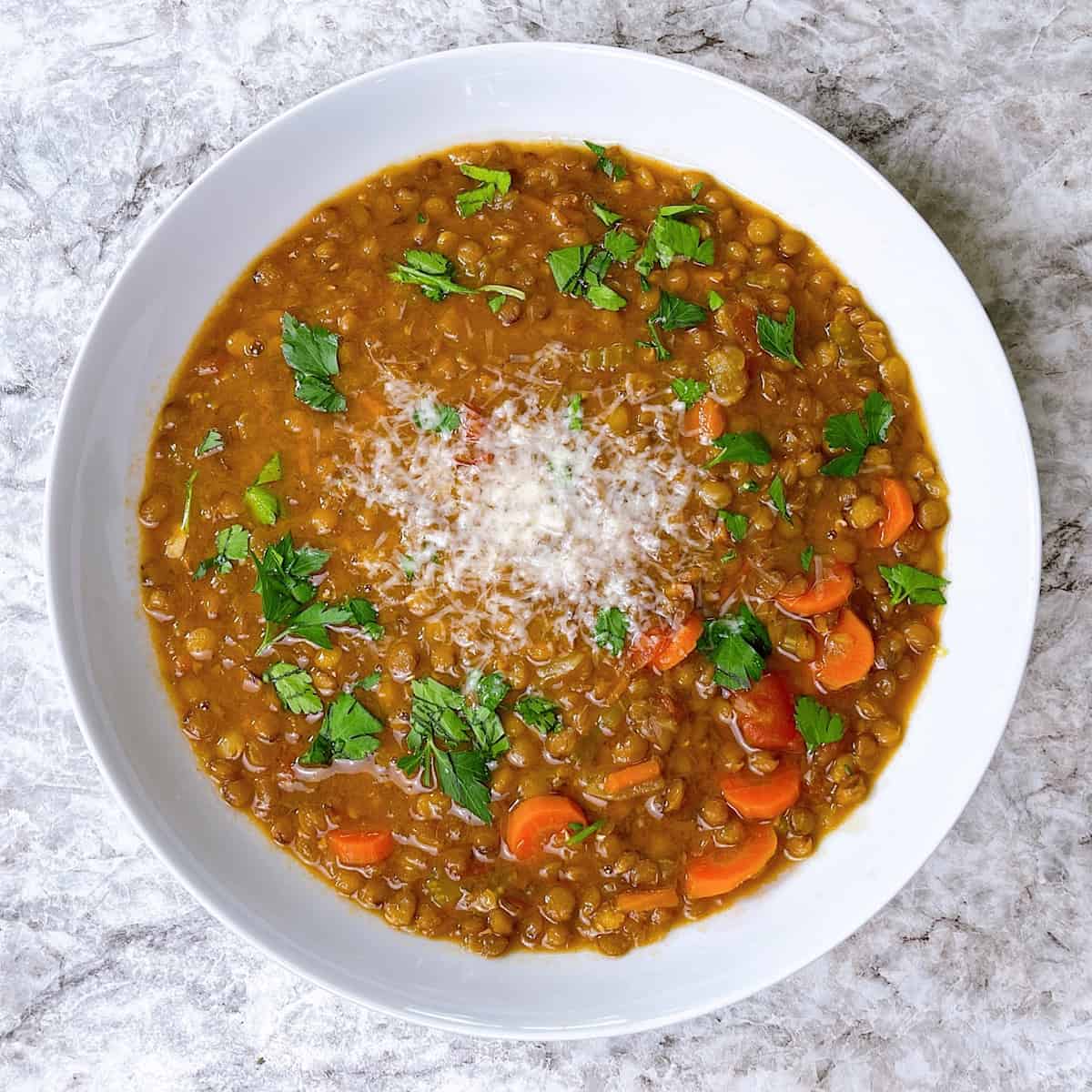 Vegan Lentil Soup topped with parsley and Parmesan in white bowl