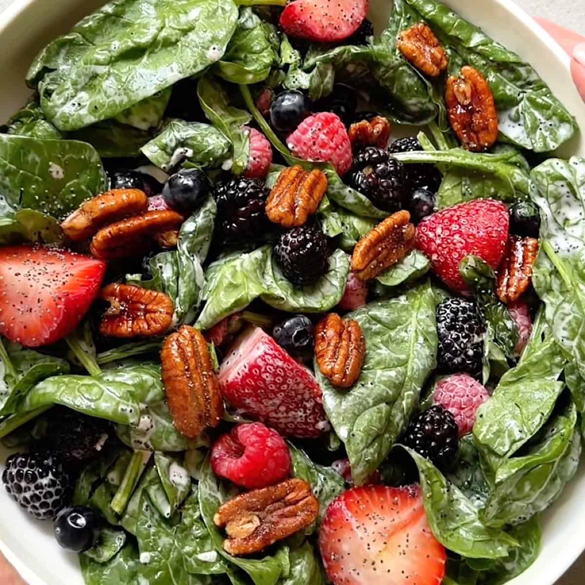 Tossed mixed berry salad in a serving bowl with candied pecans on top.