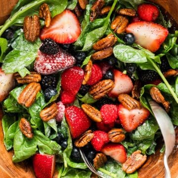 Summer berry salad with candied pecans in a wooden serving bowl.
