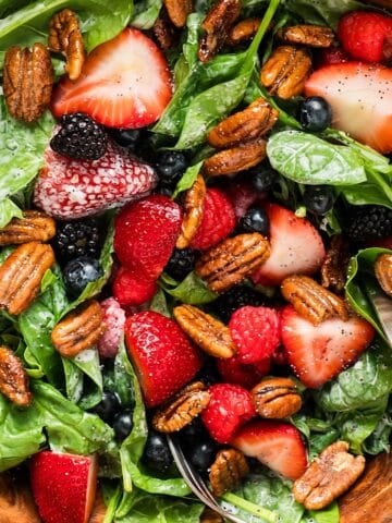 Summer berry salad with candied pecans in a wooden serving bowl.