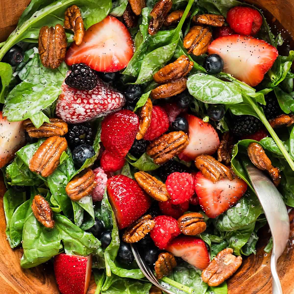 Summer berry salad with candied pecans in a wooden serving bowl.
