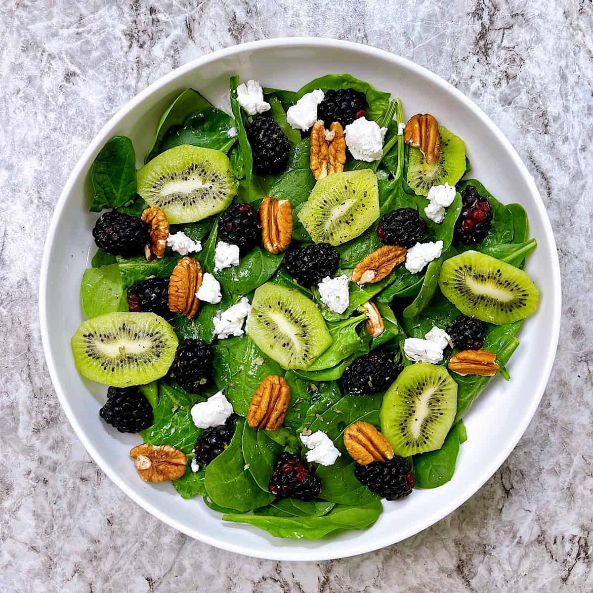 Blackberry and Kiwi Spinach Salad in white bowl and topped with pecans