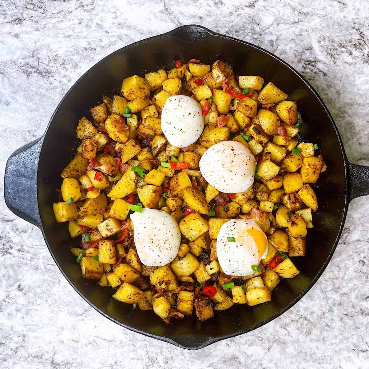 Breakfast Potatoes with Poached Eggs​ in skillet and garnished with parsley and green onion