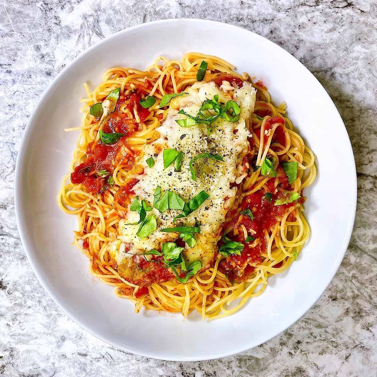Chicken Parmesan topped with basil in white bowl