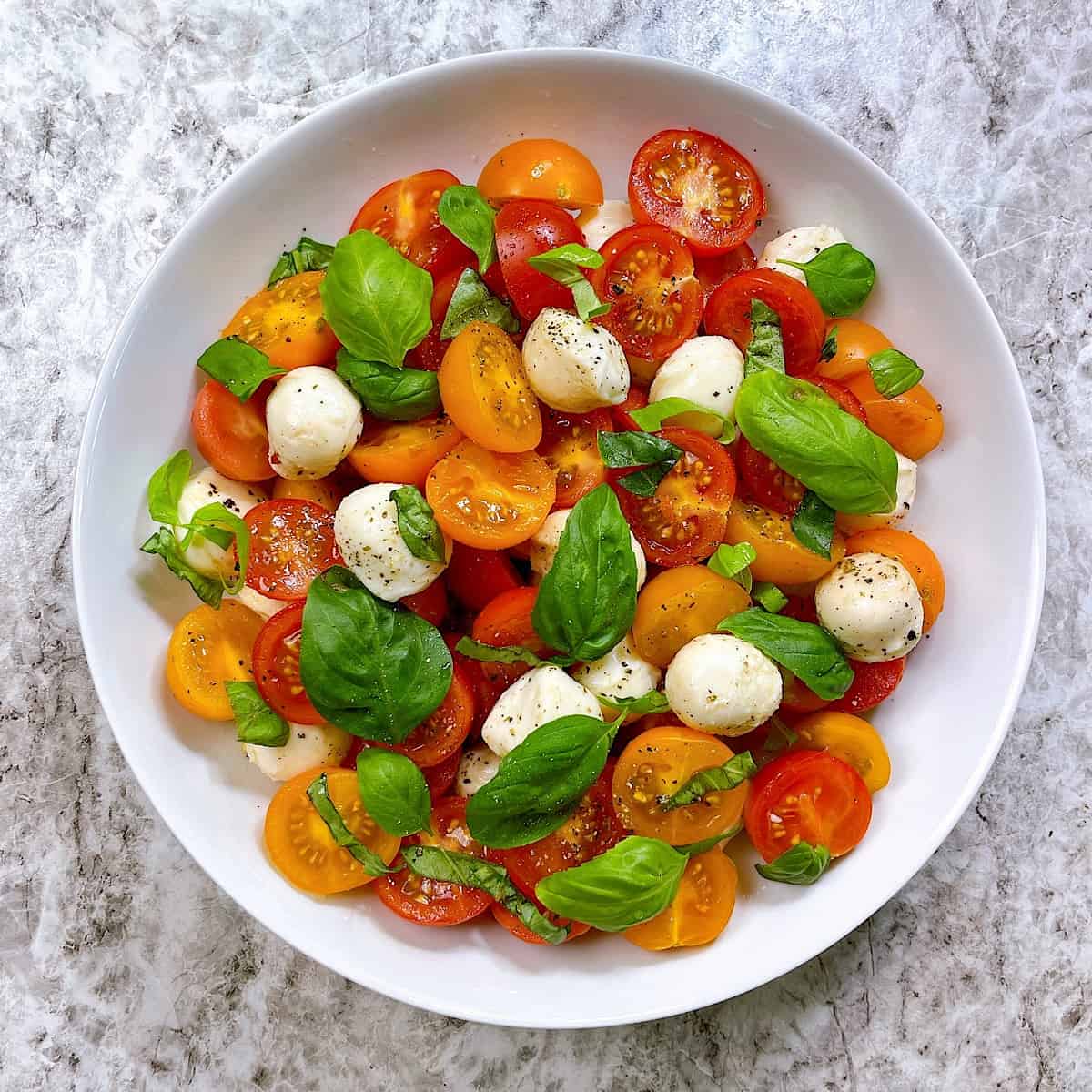 Honey Drop Tomato Caprese in white bowl topped with fresh basil