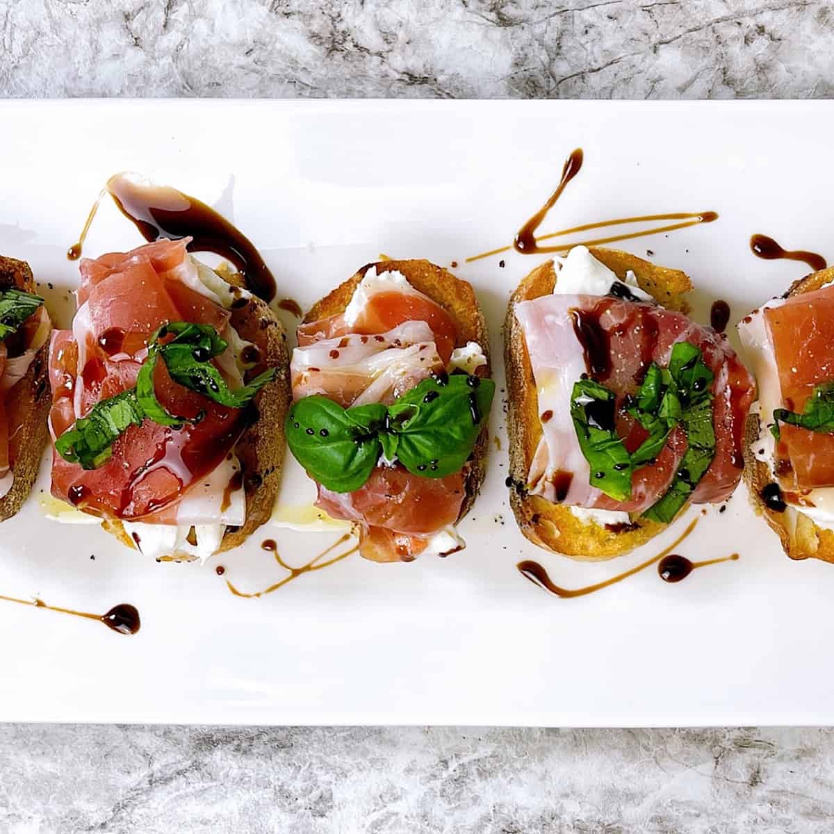 Prosciutto Burrata Crostini on white plate and drizzled with balsamic