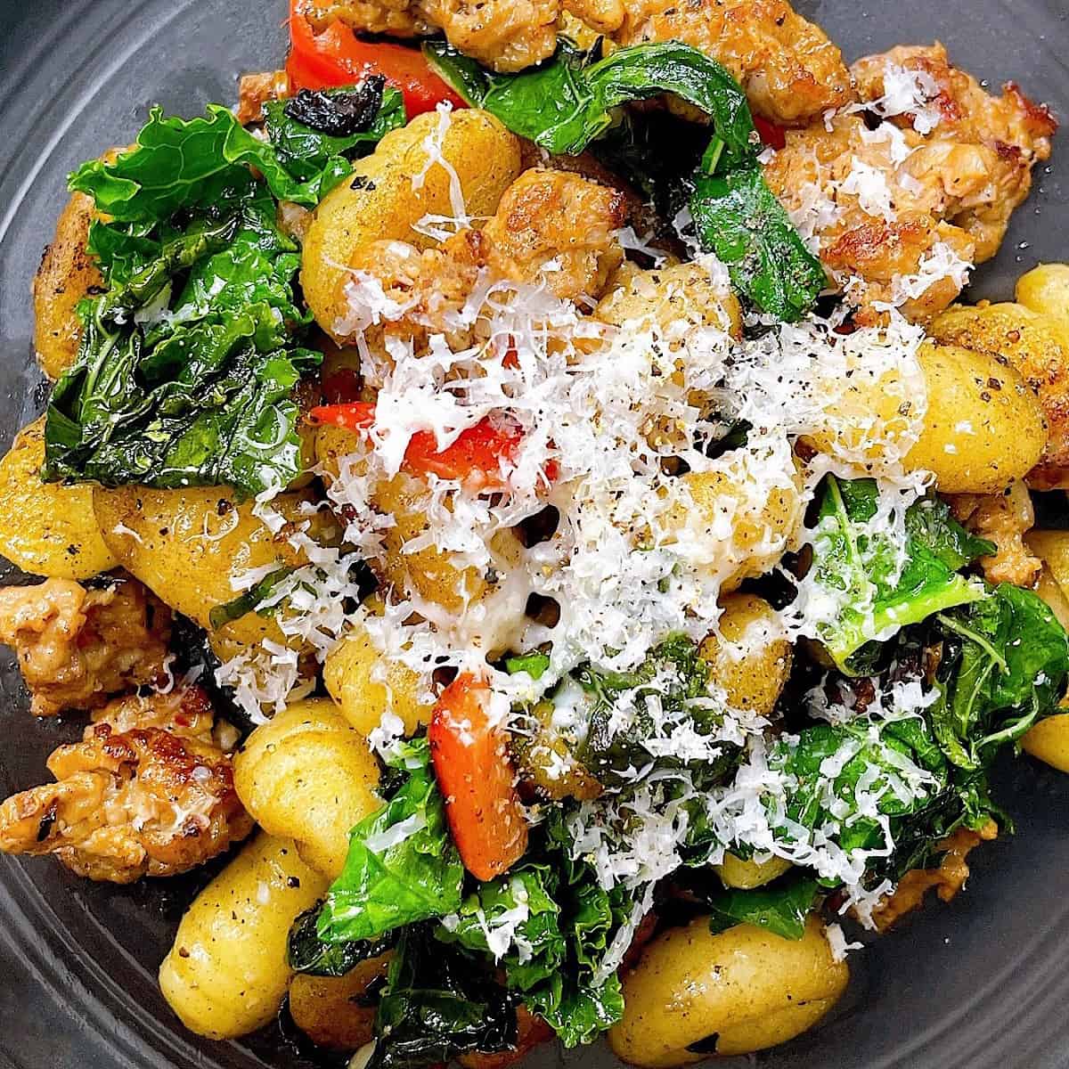 Close up of sausage and kale gnocchi on black plate with Parmesan