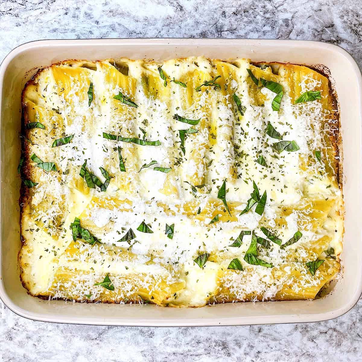 Chicken Manicotti Alfredo in casserole dish and topped with basil and Parmesan cheese