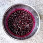 Homemade blueberry syrup simmering in a saucepan.